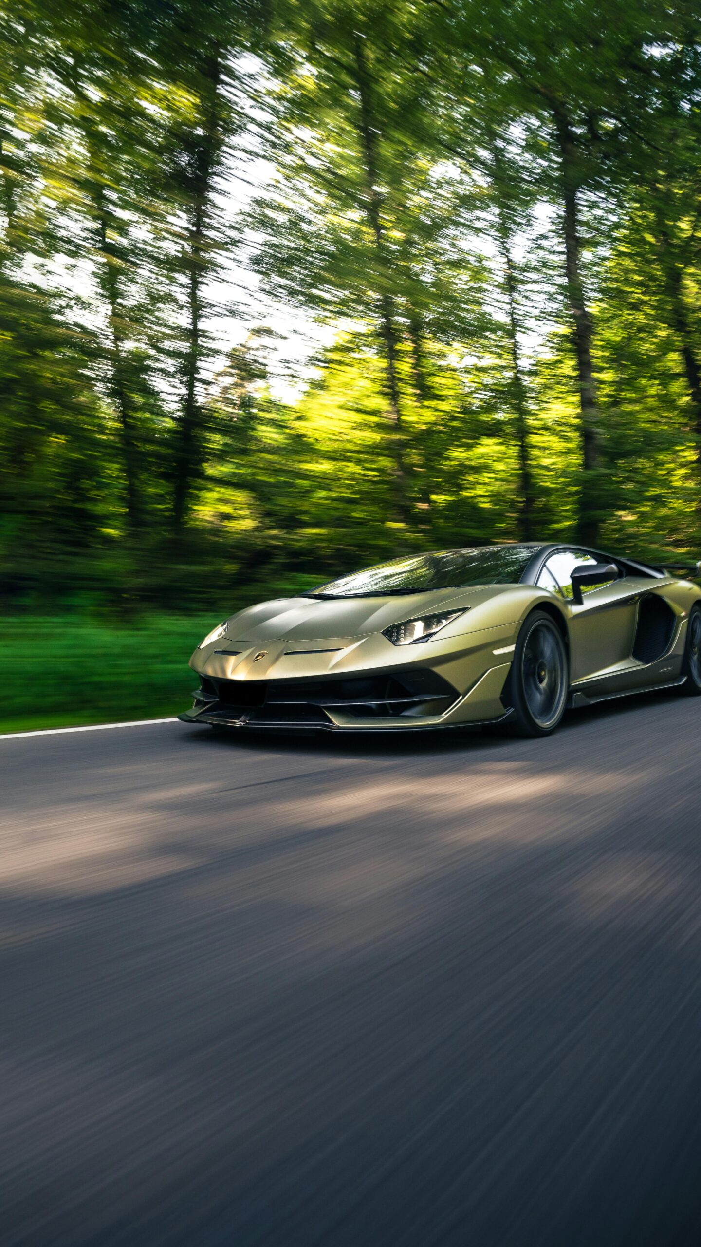 A sleek luxury car speeding on a road surrounded by lush green trees in Switzerland.