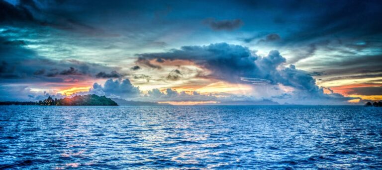 Vibrant sunset over tropical ocean with dramatic clouds and distant island.