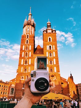 A hand holding a Polaroid camera captures St. Mary's Basilica in Krakow's Main Square, highlighting travel and culture.