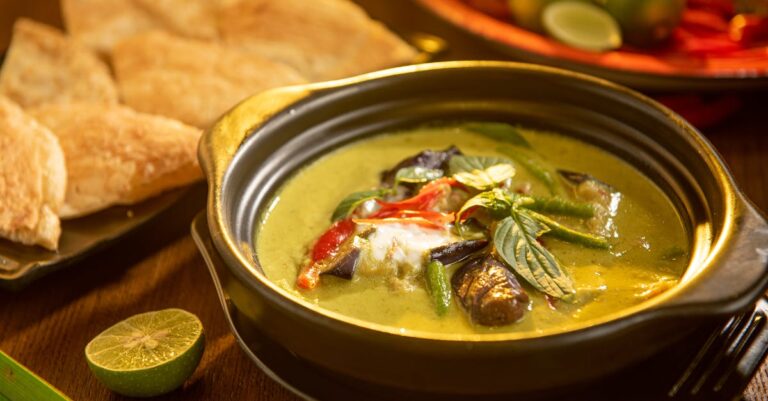 A flavorful Thai green curry with vegetables and aromatic herbs in a stylish black bowl.